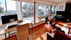 A spacious living room with a large window, a wooden desk, a comfortable sofa, and a television.