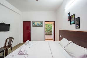 Habitación de hotel con una cama, televisor montado en la pared y una puerta que da a un balcón con vistas a zonas verdes.