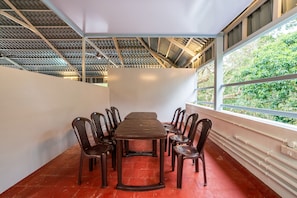 Un salón de conferencias con una larga mesa y sillas, ventanas amplias con vistas a zonas verdes y un techo alto con un diseño geométrico.