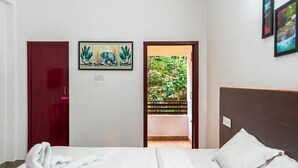 Ein Hotelzimmer mit einem Bett, einer Tür und Blick auf Grünfläche durch eine geöffnete Tür.