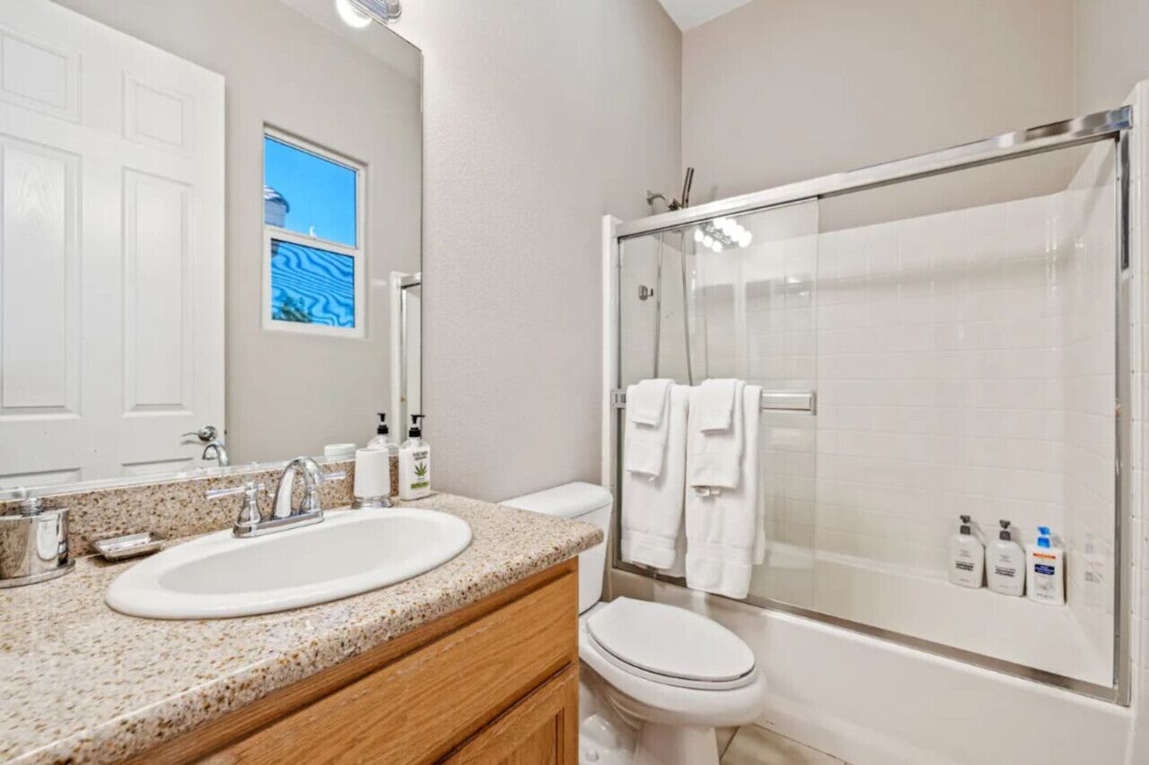 A bathroom with a double sink, toilet, and glass-enclosed shower.