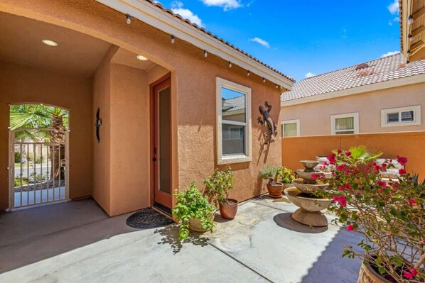 A house with a covered patio, potted plants, and a small garden area. - Cozy Casita w/ Salt water Pool, Jacuzzi & Tennis (Indio)