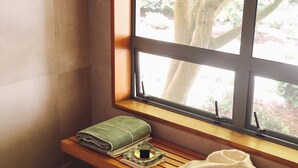 A bathroom with a bench, a towel, and a window with a view of trees. - Kumiko's Guest House (Waipara)