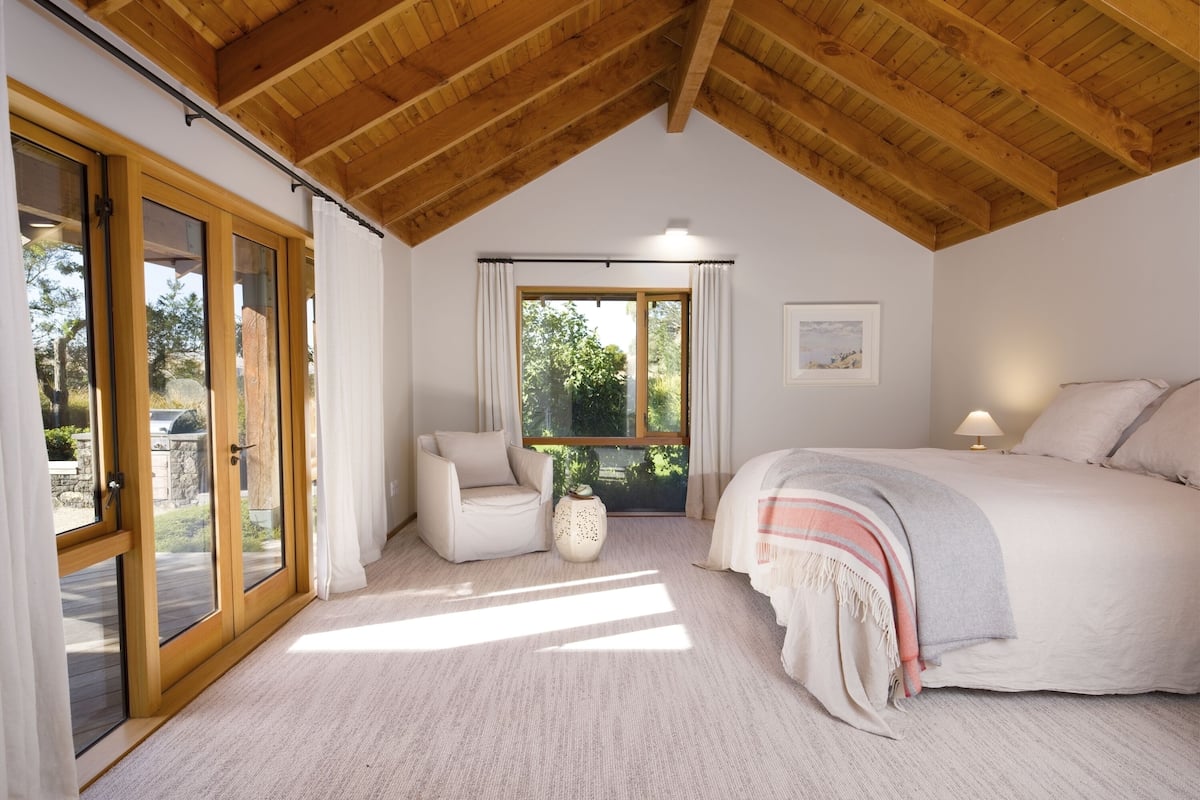 A bedroom with a large bed, a chair, a small table, and a window with curtains.