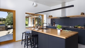 A modern kitchen with a large island, black bar stools, and a view of the outdoors. - Kumiko's Guest House (Waipara)