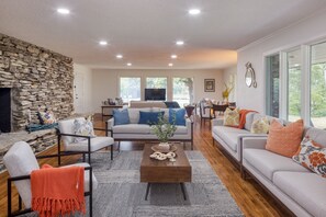 A spacious living room with a stone wall, a fireplace, and a large window providing a view of the outdoors.