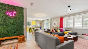 Uma sala de estar moderna com um sofá cinza, almofadas coloridas, um banco de madeira e um letreiro de neon.