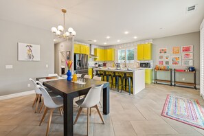 A modern kitchen with yellow cabinets, a central island, and a dining area with a dark table and white chairs.