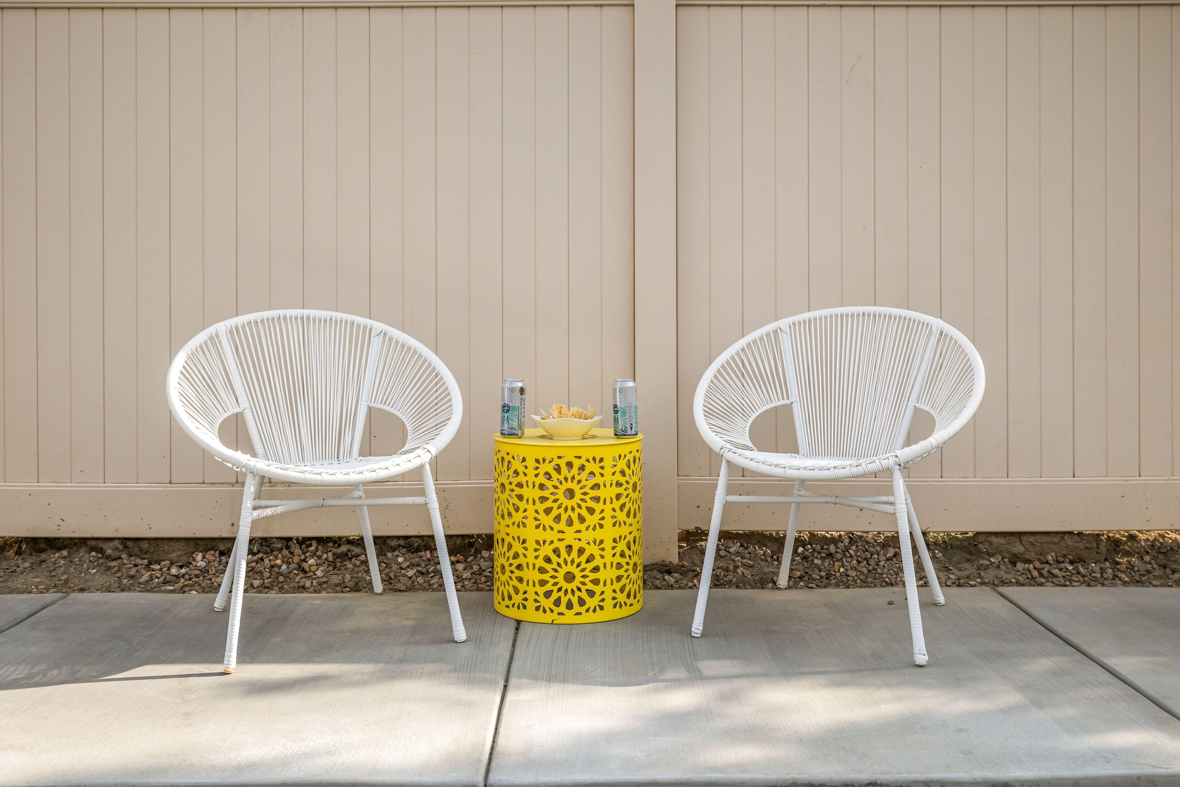 Two white wicker chairs and a yellow table with drinks in front of a beige wall.