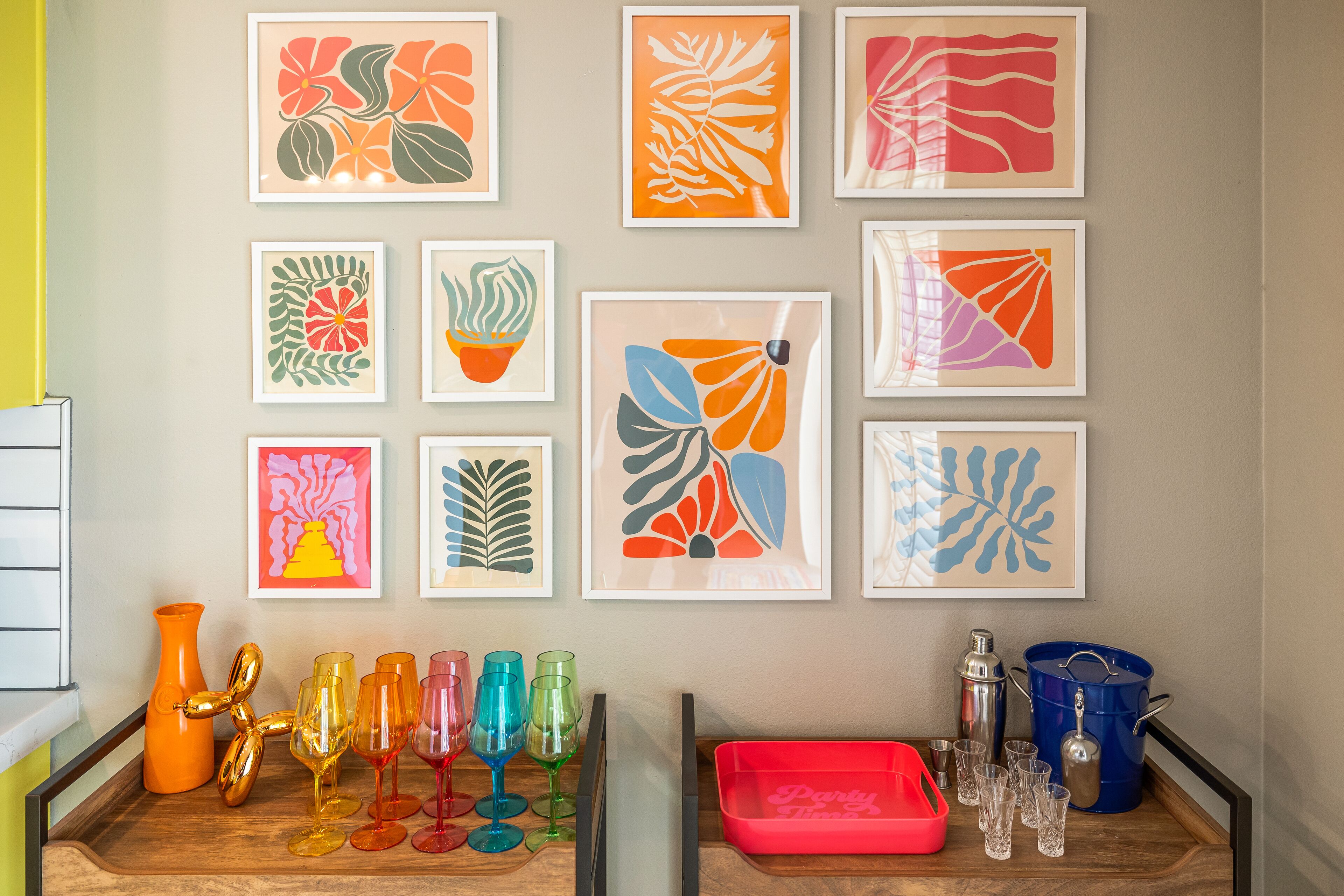 Una pared decorada con diversos cuadros, y una bandeja con vasos de colores y un recipiente rojo.