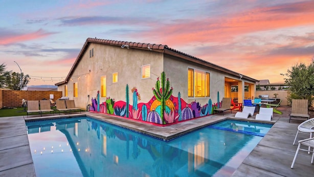 Uma casa com piscina, um mural com cactos e flores, e um pátio com espreguiçadeiras.
