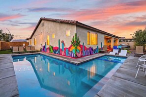 A house with a swimming pool, a mural with cacti and flowers, and a patio with lounge chairs.