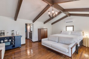 A spacious bedroom with a large bed, a sofa, wooden beams, a chandelier, and a kitchenette area. - Cozy Studio + Hot Tub | 30 Mins to Knoxville | Amber Cabin (New Market)