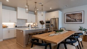 Una cocina moderna con armarios blancos, una isla de madera y una zona de comedor con una mesa grande y sillas.
