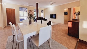 A spacious dining area with a large table and chairs, a ceiling fan, and a television mounted on the wall.