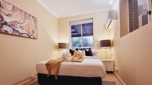 A bedroom with a bed, two bedside tables, a window, and an air conditioning unit.