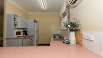 A kitchen with a pink countertop, white cabinets, a microwave, a refrigerator, a sink, and a potted plant.