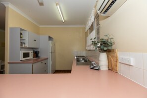 A kitchen with a pink countertop, white cabinets, a microwave, a refrigerator, a sink, and a potted plant. - Fishing Dreams & Coastal Scenes in Onslow (Onslow)