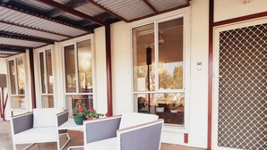A covered outdoor seating area with a table and two chairs, a potted plant, and a view through large windows.