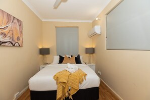 A hotel room with a bed, bedside lamps, an air conditioning unit, a painting on the wall, and a window. - Fishing Dreams & Coastal Scenes in Onslow (Onslow)