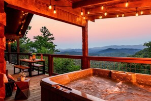 A hot tub with a wooden deck and a table with chairs, overlooking a mountainous landscape. - BEST MTN VIEWS|Couples|Private|Firepit|Romantic| (Sevierville)