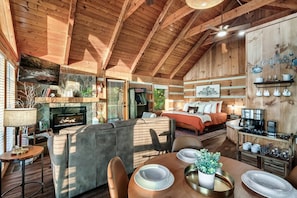 A cozy cabin interior with a fireplace, a dining area, a bed, and a coffee station.