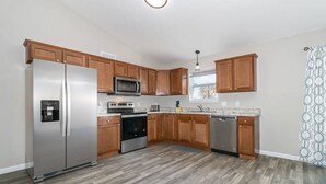 A modern kitchen with wooden cabinets, stainless steel appliances, and a herringbone-patterned floor. - BRAND NEW home among the Nook in Hamilton, OH (Hamilton)