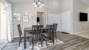 A dining area with a table and chairs, a patterned rug, a ceiling light fixture, and a television mounted on the wall. - BRAND NEW home among the Nook in Hamilton, OH (Hamilton)