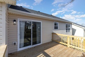 A single-story house with a wooden deck, a sliding glass door, and a small porch with a railing.