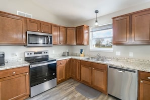 A kitchen with wooden cabinets, stainless steel appliances, a granite countertop, and a window with a view.
