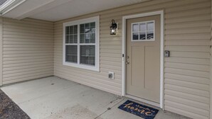 A house with a beige exterior, a front door, a window with blinds, a porch, and a doormat. - BRAND NEW Home away from Home among the Nook (Hamilton)