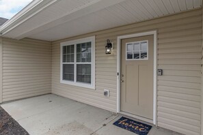 A house with a beige exterior, a front door, a window with blinds, a porch, and a doormat. - BRAND NEW Home away from Home among the Nook (Hamilton)
