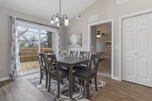 A dining area with a table and chairs, a chandelier, a painting on the wall, and a door leading to another room. - BRAND NEW Home away from Home among the Nook (Hamilton)