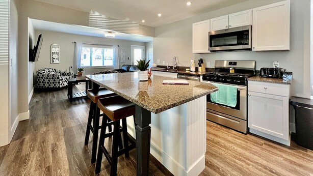 A modern kitchen with a central island, stainless steel appliances, and a dining area with a sofa and chairs.