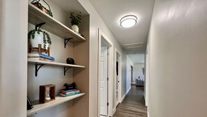 A narrow hallway with white walls, wooden flooring, and built-in shelving units.
