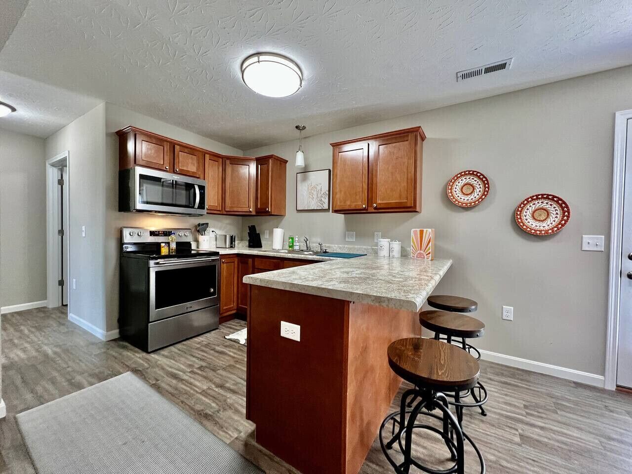 A modern kitchen with wooden cabinets, a built-in microwave, and a central island with stools.