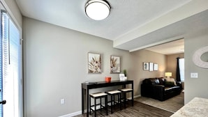 A living room with a black sofa, a coffee table, and a dining area with a black table and three chairs. - 430 Ridgelawn · Brand New Home Walking distance to Spooky Nook (Hamilton)