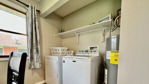 Un lavadero equipado con dos lavadoras, una secadora, un lavadero y una ventana con cortinas.