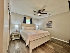 Une chambre à coucher avec un lit, des tables de chevet, un ventilateur de plafond et un tableau au mur.