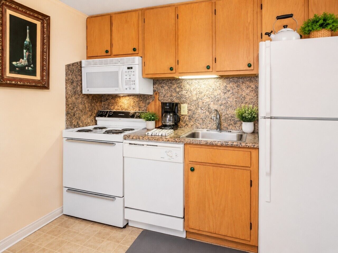 A compact kitchen with wooden cabinets, a white stove, a microwave, a coffee maker, and a refrigerator.