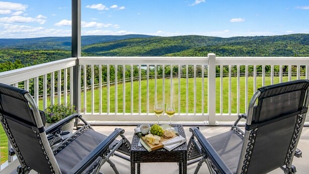 Un balcon avec deux chaises, une table avec une bouteille de vin et une vue sur des collines verdoyantes.