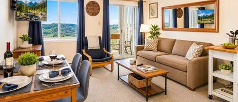 Una sala de estar con sofá, una mesa de comedor para dos personas, televisión y vistas al exterior.