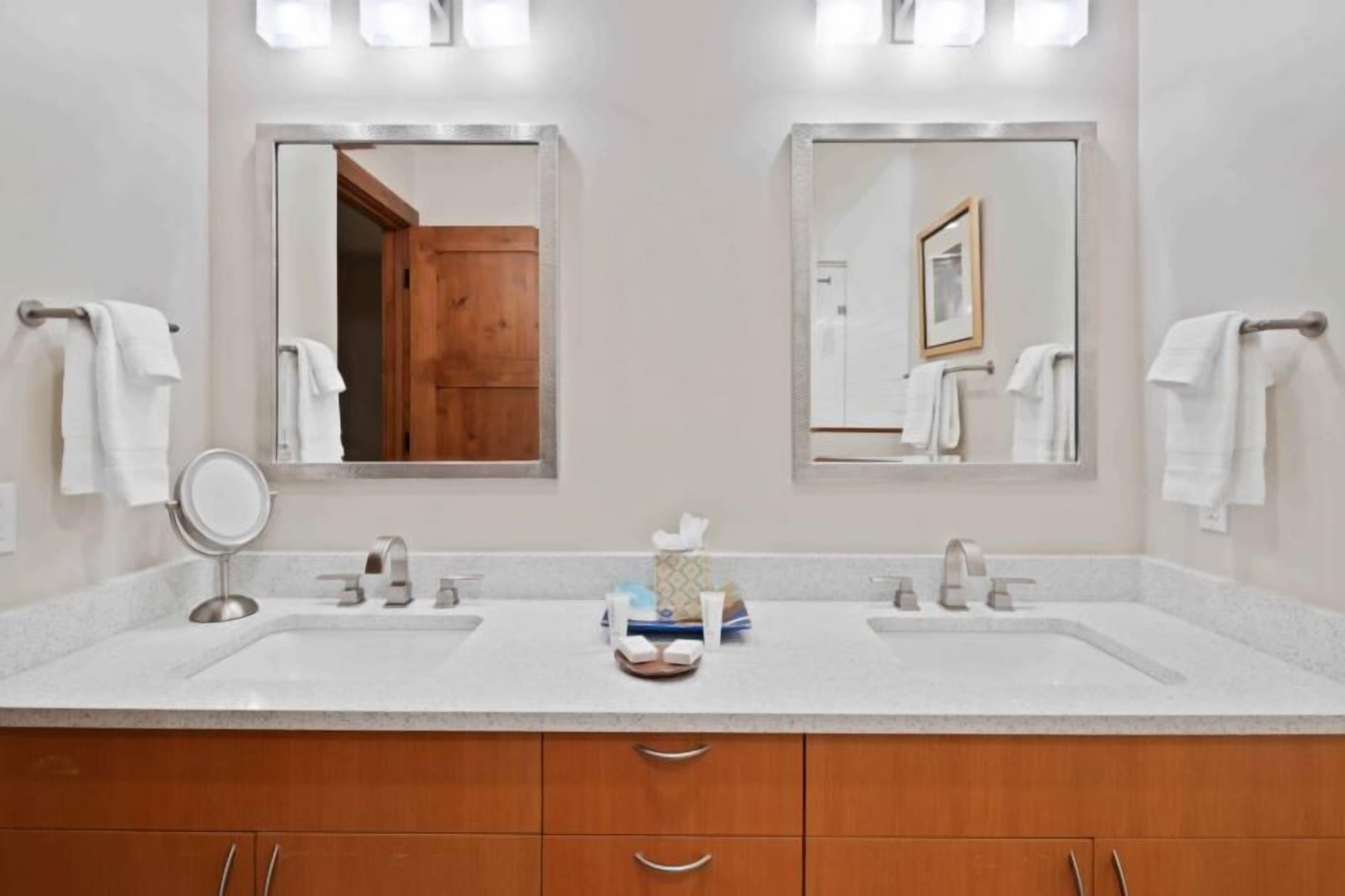 Une salle de bain moderne avec deux lavabos, un miroir rond et des meubles en bois.