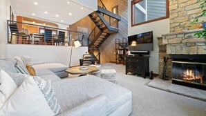 A spacious living room with a fireplace, a staircase, and a television. - Ridgepoint Townhome 142 - 3.5 Bedroom plus Loft Residence (Avon)