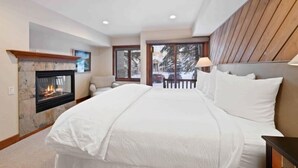 A bedroom with a fireplace, a large bed, a view of the outdoors, and a wooden ceiling. - Ridgepoint Townhome 142 - 3.5 Bedroom plus Loft Residence (Avon)