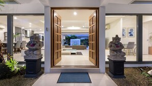 A modern entrance with a glass door leading to a living area, featuring two stone statues and a blue mat at the entrance. - Bella Beach House | Port Douglas (PORT DOUGLAS)