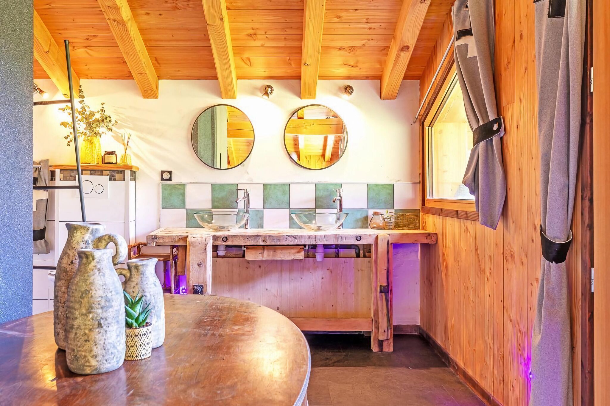 A rustic kitchen with wooden beams, a wooden countertop, and a window with curtains.