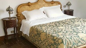 A bed with a patterned bedspread, a wooden headboard, two bedside tables with lamps, and a tiled floor.