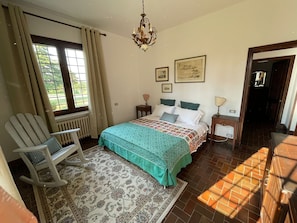 Une chambre à coucher avec un lit, une chaise, un lustre, un radiateur, une fenêtre et une porte.