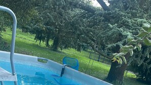 An above-ground swimming pool with a ladder, surrounded by grass and trees.